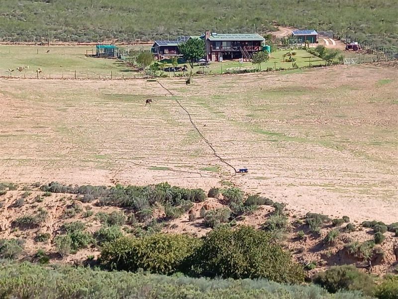 An elevated aerial view of a rural farm property featuring a main dwelling, outbuildings, and expansive surrounding grazing land.