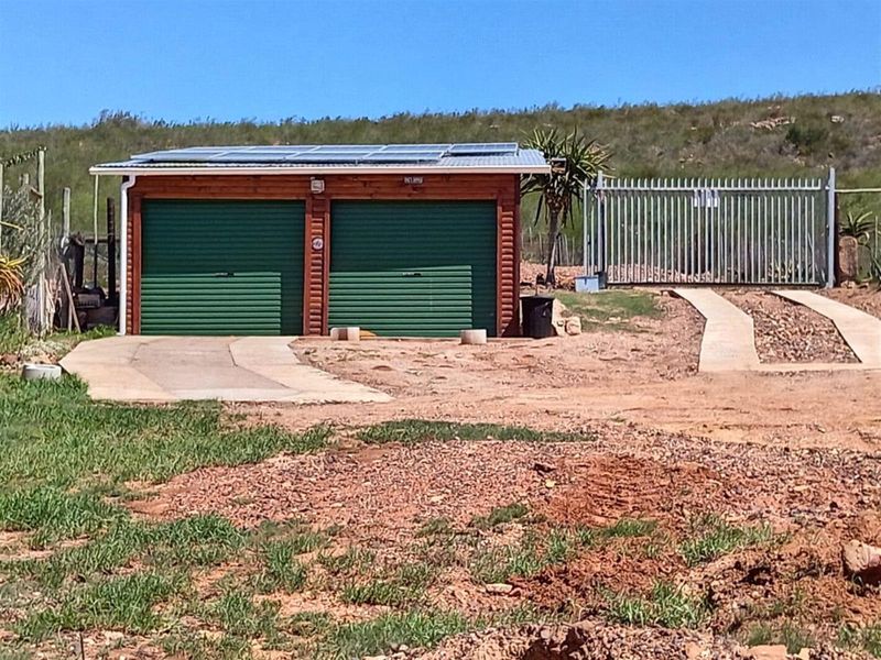 A detached double garage featuring green roller doors, solar panels on the roof, and an adjacent gated entrance on a rural farm property.