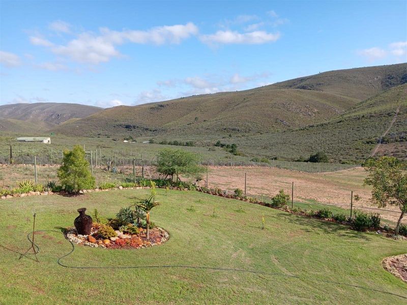 Expansive rural landscape view overlooking a well-maintained garden with a landscaped succulent bed and perimeter fencing, set against a backdrop of rolling hills.