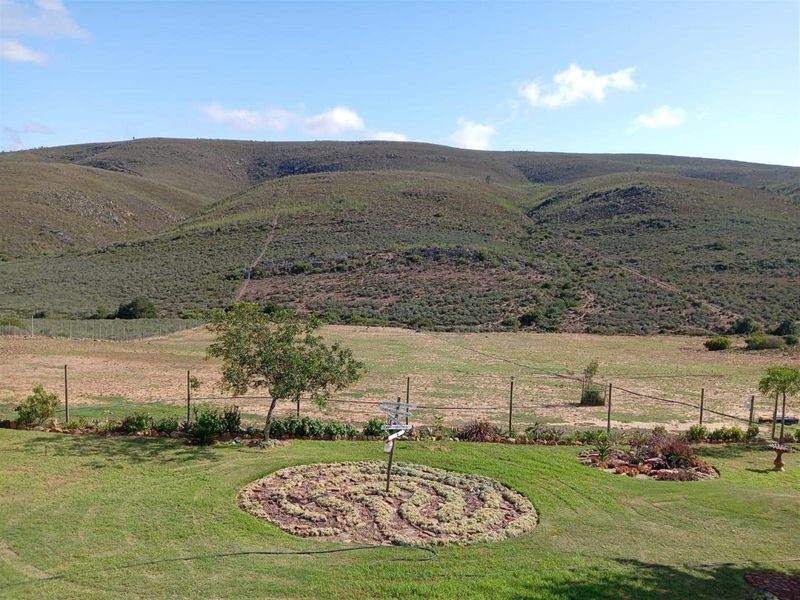 A scenic view of the expansive farm landscape, featuring a manicured lawn, a decorative stone garden feature, and rolling hills in the background.