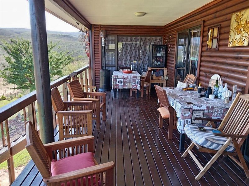 A spacious covered wooden deck featuring log-style wall cladding, offering expansive views of the surrounding farm landscape.