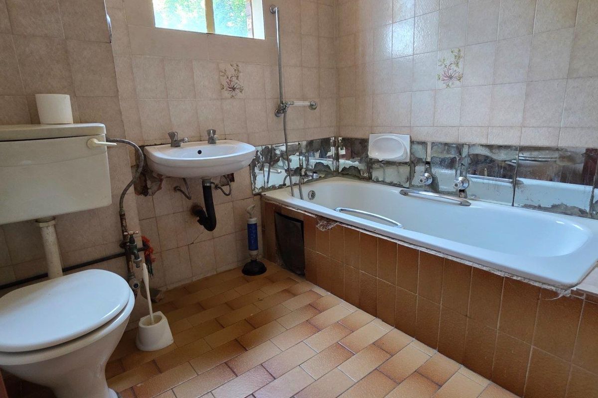 A dated bathroom featuring a standard bathtub, pedestal sink, and toilet with original tiled finishes requiring modernization and repair.