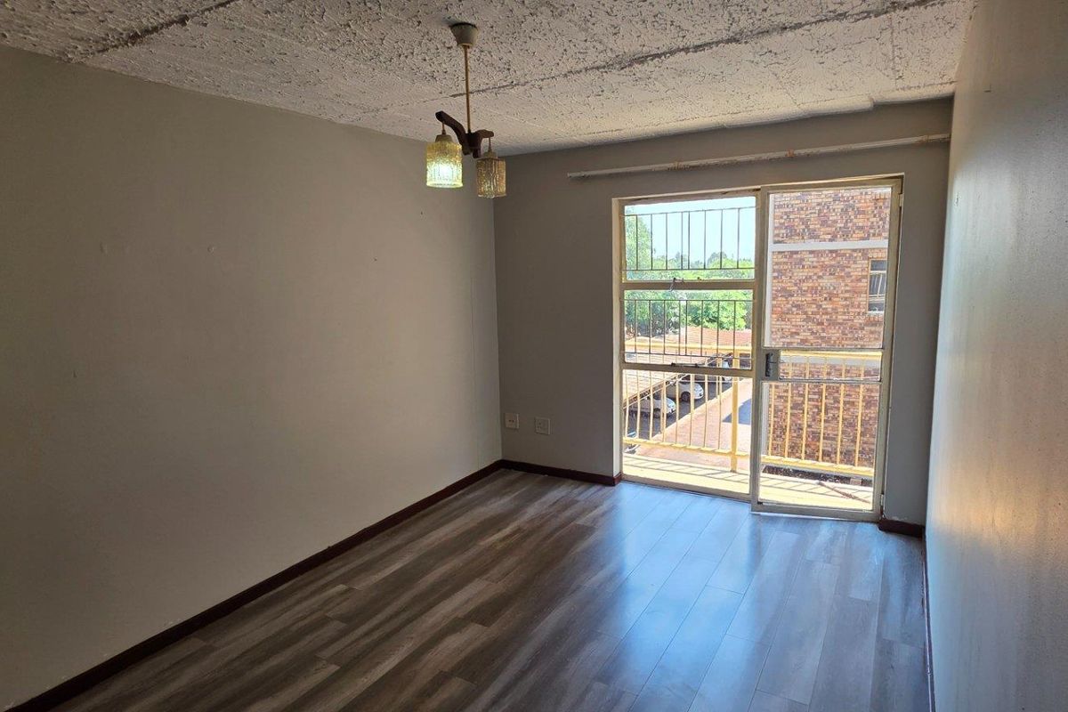 An empty bedroom featuring laminate flooring, a textured ceiling, and a sliding glass door with a security gate leading to a balcony.