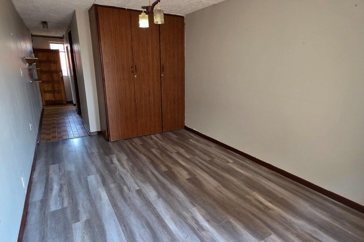 A vacant bedroom featuring modern laminate flooring and a built-in wooden wardrobe, offering a clean and neutral space ready for personalization.