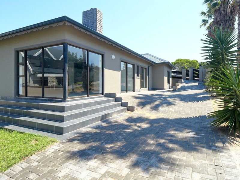 Rear exterior view featuring a paved driveway, stone-clad base, chimney, and tiled steps leading to large sliding glass doors.