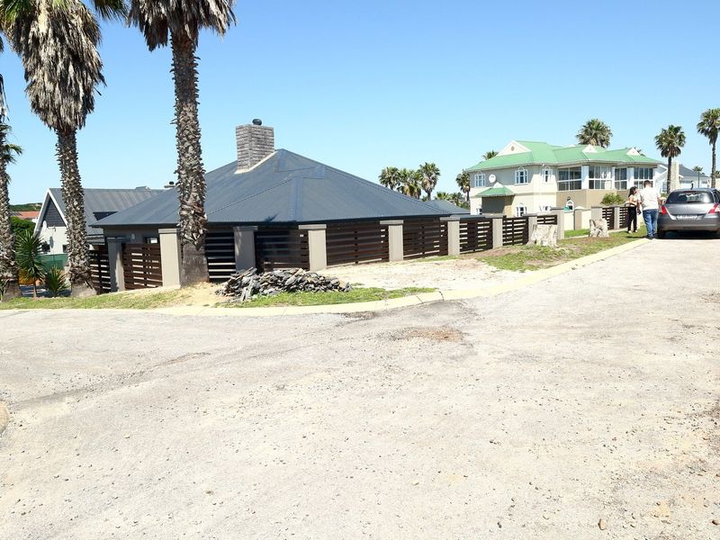 Street view showing the approach to the property with a metal roof structure, boundary fencing, and unpaved road access.