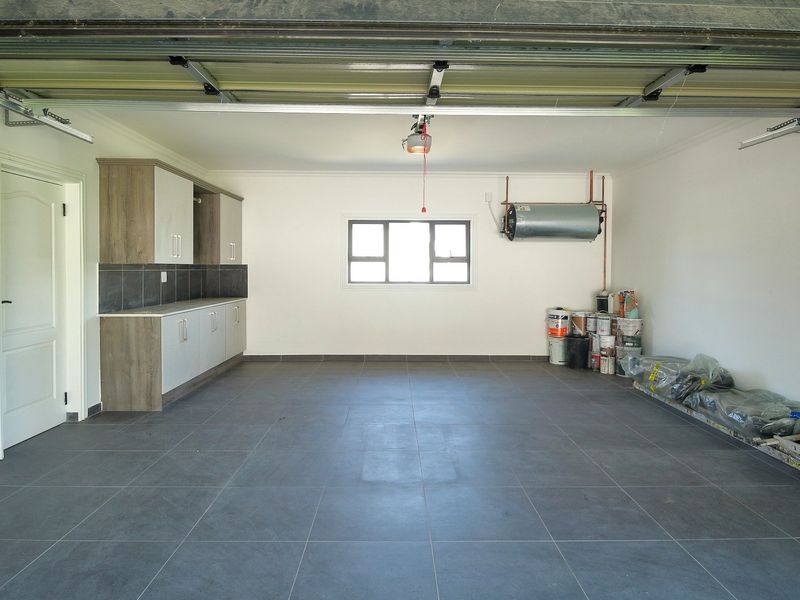 Spacious double garage featuring tiled flooring, built-in storage cabinetry, and an installed electric geyser, providing ample space for vehicles and additional utility storage.