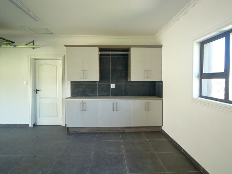 A clean, well-maintained garage featuring tiled flooring, built-in storage cabinetry with a tiled splashback, and a functional garage door mechanism.