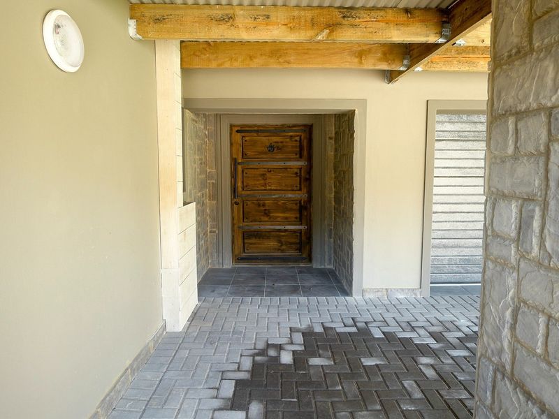 A covered entrance area featuring a solid timber front door, exposed wooden beams, and stone cladding accents with paved flooring.