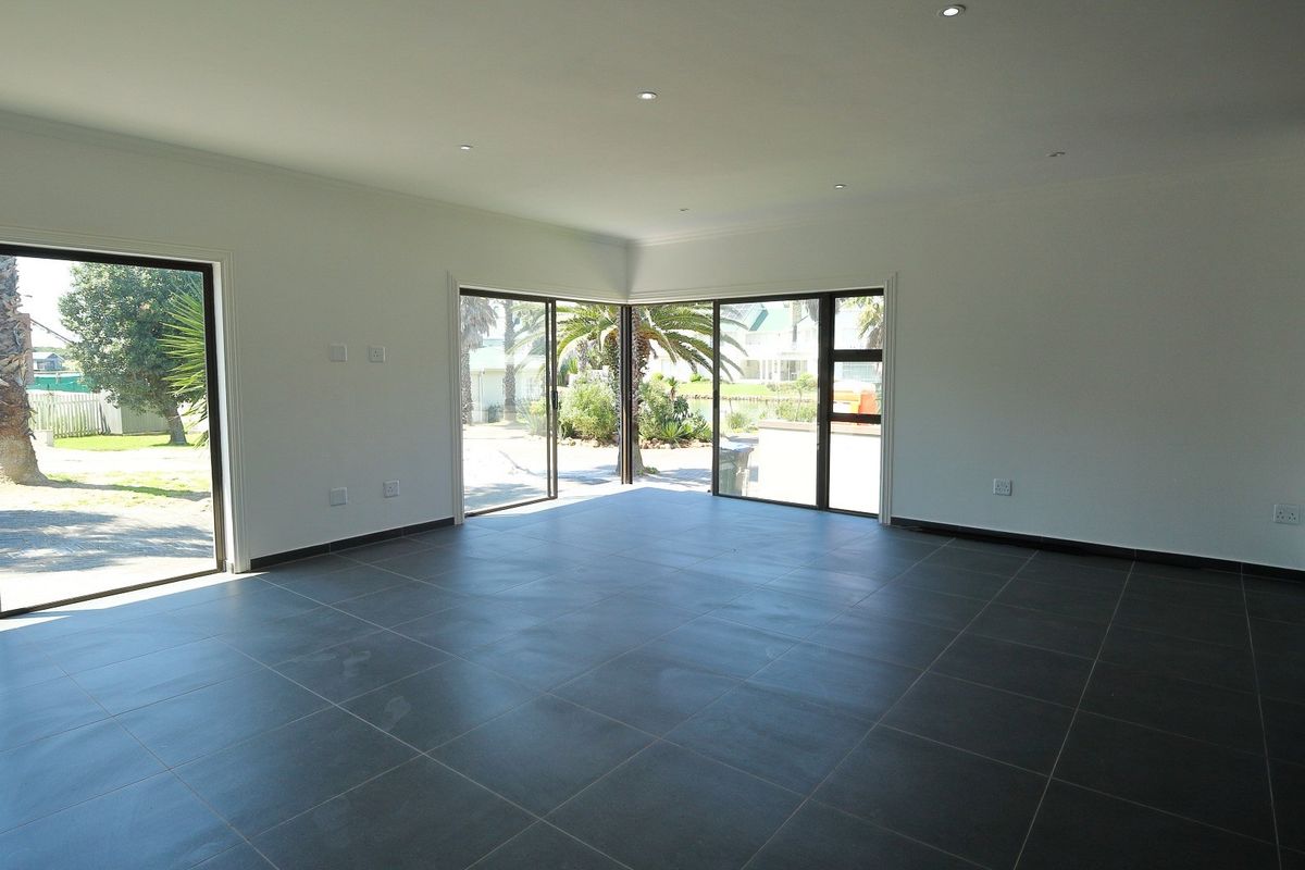 Spacious, light-filled living area featuring large format floor tiles, recessed downlights, and expansive sliding glass doors providing seamless access to the garden.