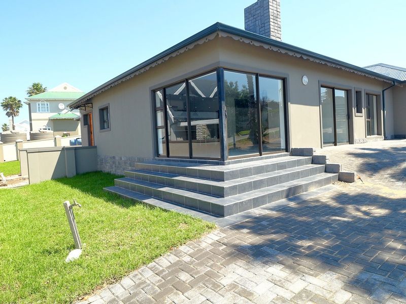 Rear exterior view of the house featuring a paved driveway, tiled patio steps, and large sliding glass doors leading into the living area.