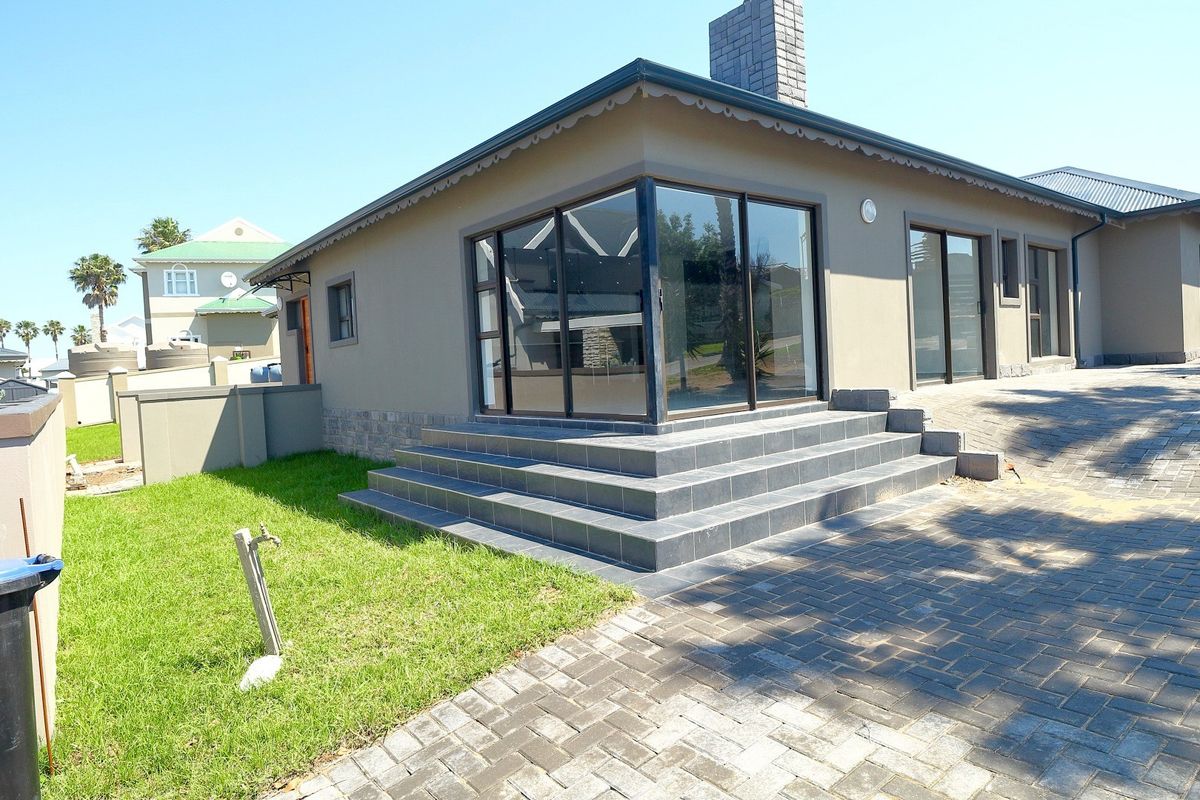 Rear exterior view of the house featuring a paved driveway, tiled patio steps, and large sliding glass doors leading into the living area.