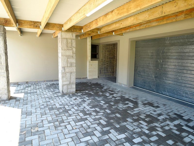 A well-maintained covered carport area featuring stone-clad pillars, exposed timber beams, and a paved driveway leading to a secure roll-up garage door.