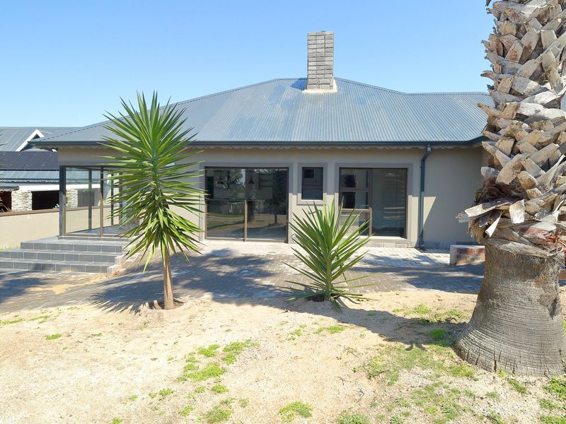 Rear view of the house featuring a paved patio area, sliding glass doors, and a corrugated metal roof with a brick chimney.