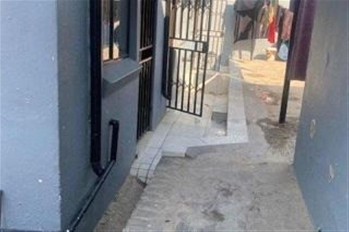 A narrow exterior side passage featuring a security gate, tiled step, and concrete paving leading to the rear of the property.