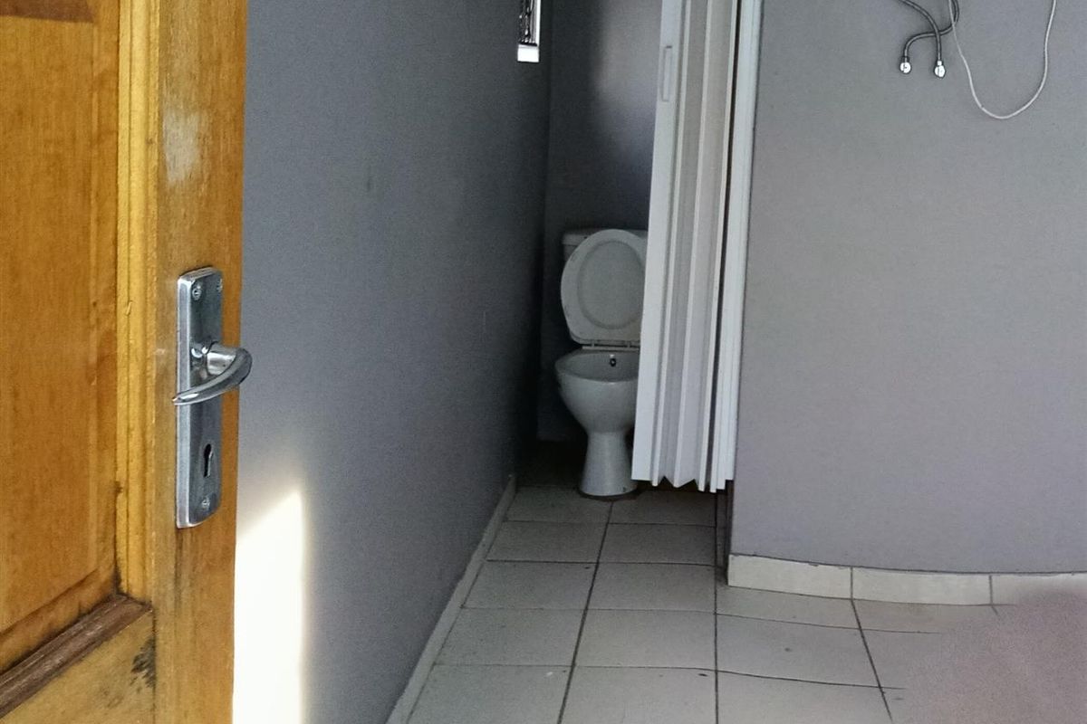 A small bathroom featuring tiled flooring, a toilet, and an electric water heater unit mounted on the wall.