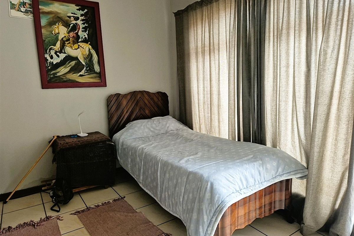 A bedroom featuring tiled flooring and large windows with floor-to-ceiling curtains, providing natural light to the space.