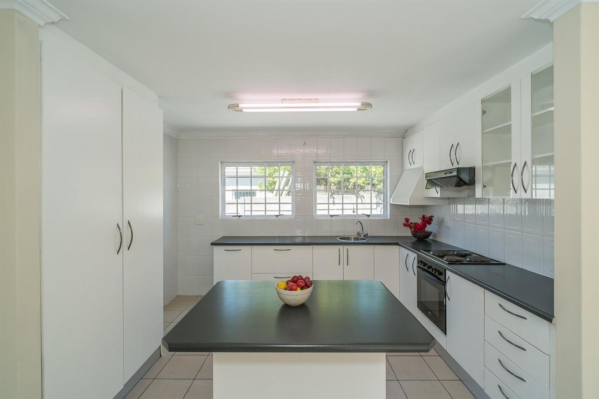 A clean, functional kitchen featuring white cabinetry, black countertops, a built-in oven, hob, and extractor fan with tiled finishes throughout.