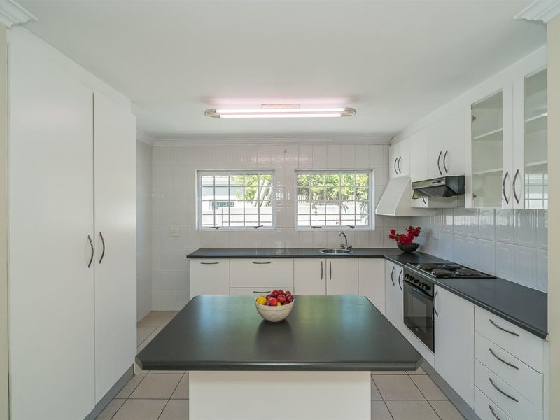 A clean, functional kitchen featuring white cabinetry, black countertops, a built-in oven, hob, and extractor fan with tiled finishes throughout.
