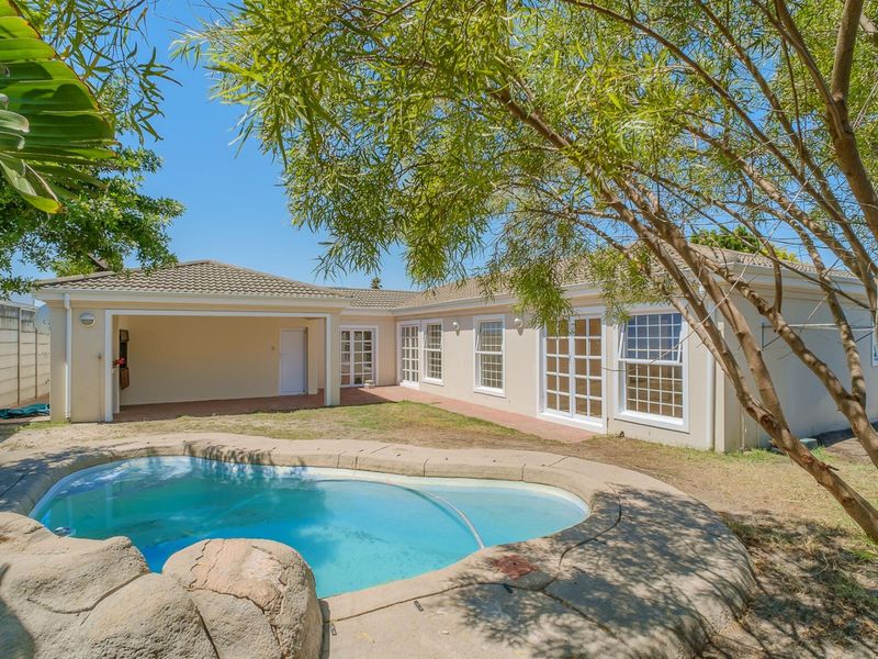 Rear exterior view featuring a swimming pool with rock-style coping, a covered patio area, and direct access to the home via multiple sets of french doors.