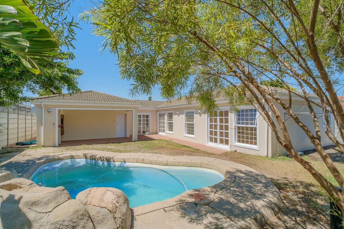 Rear exterior view featuring a swimming pool with rock-style coping, a covered patio area, and direct access to the home via multiple sets of french doors.