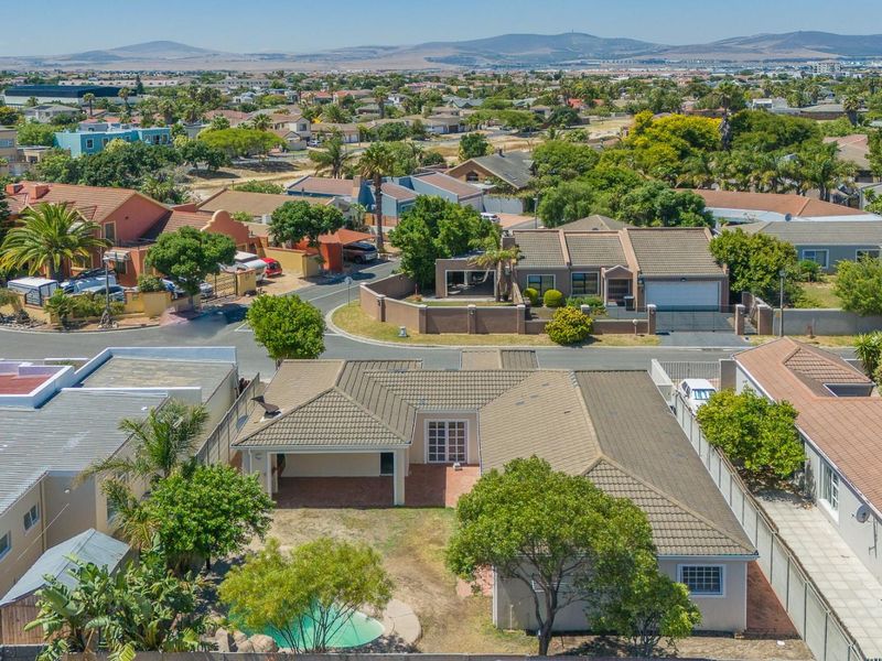 Aerial view of the property showing the tiled roof, swimming pool, paved patio area, and surrounding residential neighborhood.