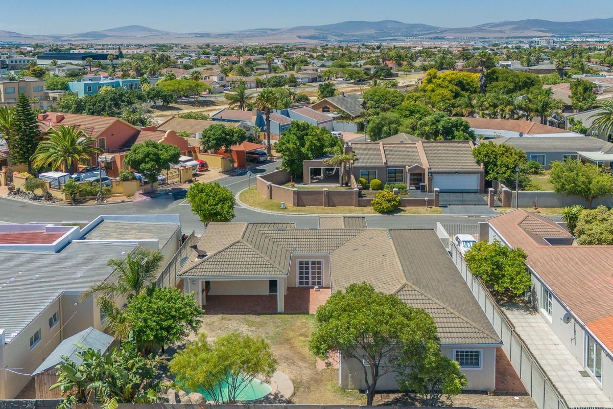 Aerial view of the property showing the tiled roof, swimming pool, paved patio area, and surrounding residential neighborhood.