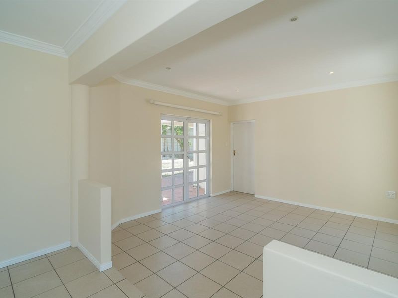 A bright, empty living area featuring neutral tiled flooring, recessed lighting, and glass-paned french doors leading to the exterior.