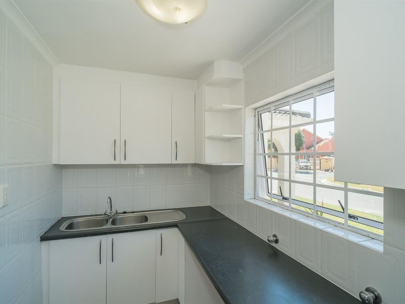 A functional scullery featuring white built-in cabinetry, a double bowl stainless steel sink, dark laminate countertops, and tiled splashbacks.