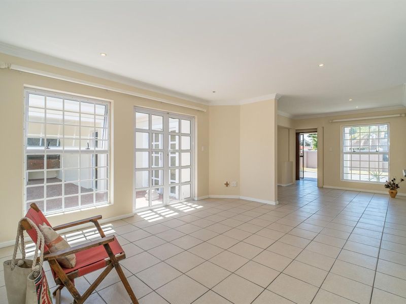 Spacious, light-filled living area featuring neutral tiled flooring, recessed lighting, and multiple windows and french doors providing access to the exterior.