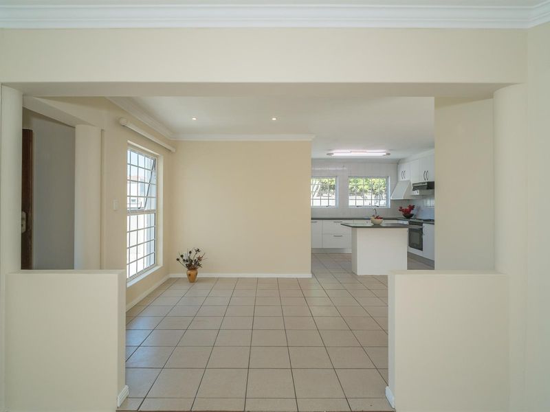 An open-plan living and kitchen area featuring neutral tiled flooring, white cabinetry, and a central kitchen island with built-in appliances.