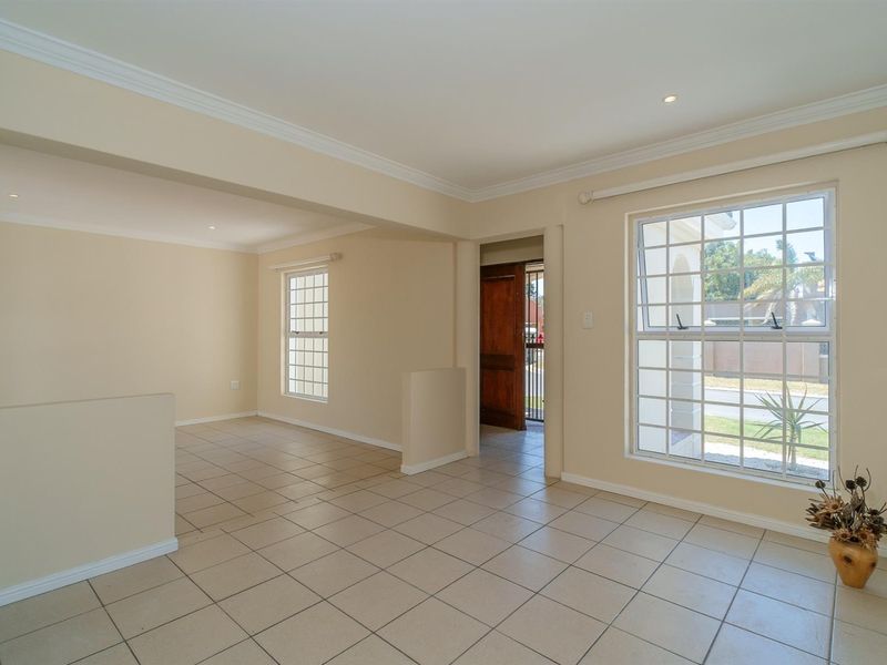 A bright, open-plan living area featuring neutral tiled flooring, recessed lighting, and large grid-pattern windows, providing a clean and versatile space.