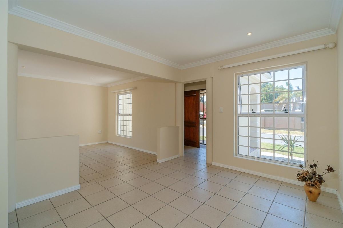 A bright, open-plan living area featuring neutral tiled flooring, recessed lighting, and large grid-pattern windows, providing a clean and versatile space.