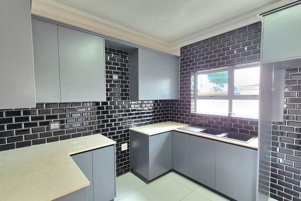 Modern kitchen featuring sleek grey cabinetry, contrasting black subway tile backsplash, stone countertops, and a double basin sink with a black mixer tap.
