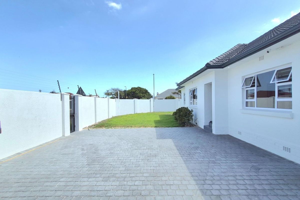A well-maintained rear exterior featuring a paved driveway, lawn area, and secure perimeter wall with electric fencing.