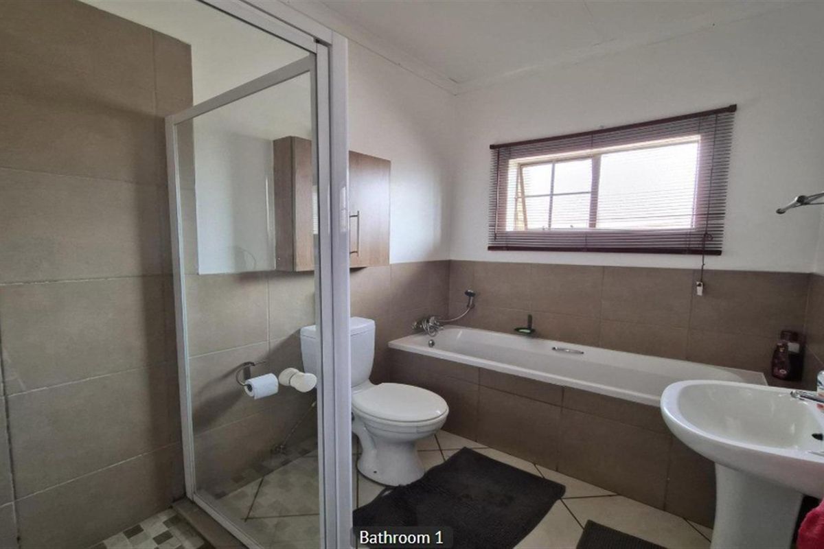 A functional bathroom featuring a separate shower enclosure, a built-in bathtub, a pedestal sink, and neutral wall tiling.