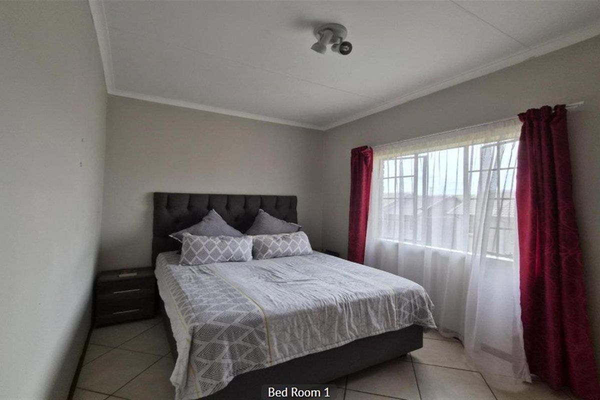 A well-lit bedroom featuring neutral wall tones, tiled flooring, and a large window allowing for natural light.
