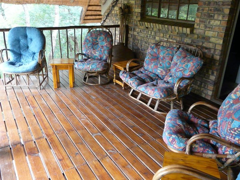 A covered patio area featuring timber decking, rustic face-brick walls, and a thatched roof overhang, providing a natural outdoor living space.