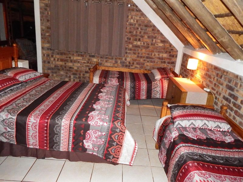 A rustic bedroom featuring exposed brick walls, tiled flooring, and a pitched roof with visible timber rafters.