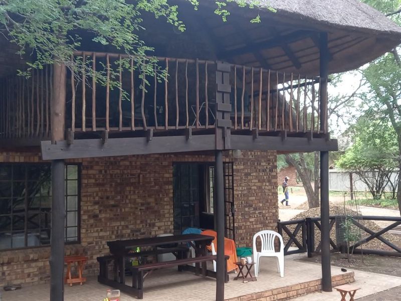 A two-story brick house featuring a thatched roof and a covered ground-floor patio with an overhead wooden balcony.