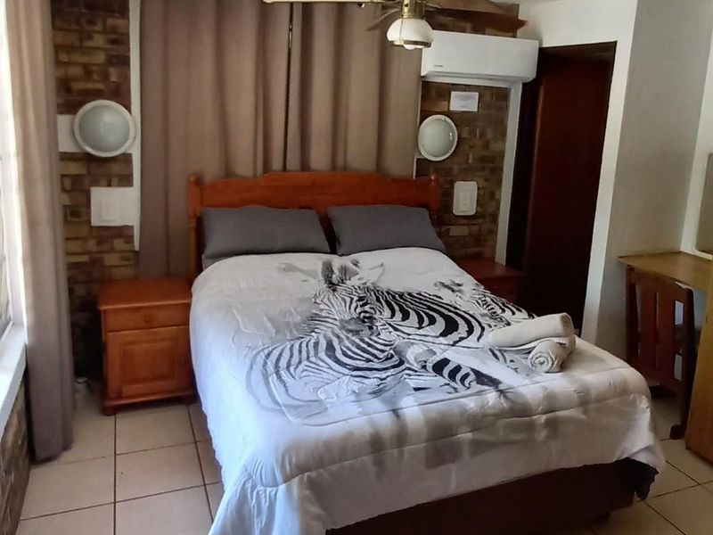 A bedroom featuring a brick feature wall, ceiling fan, and wall-mounted air conditioning unit with tiled flooring.