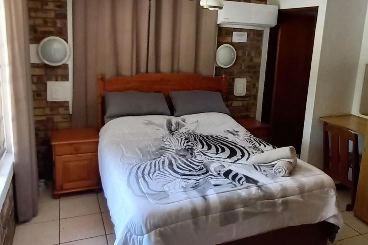 A bedroom featuring a brick feature wall, ceiling fan, and wall-mounted air conditioning unit with tiled flooring.
