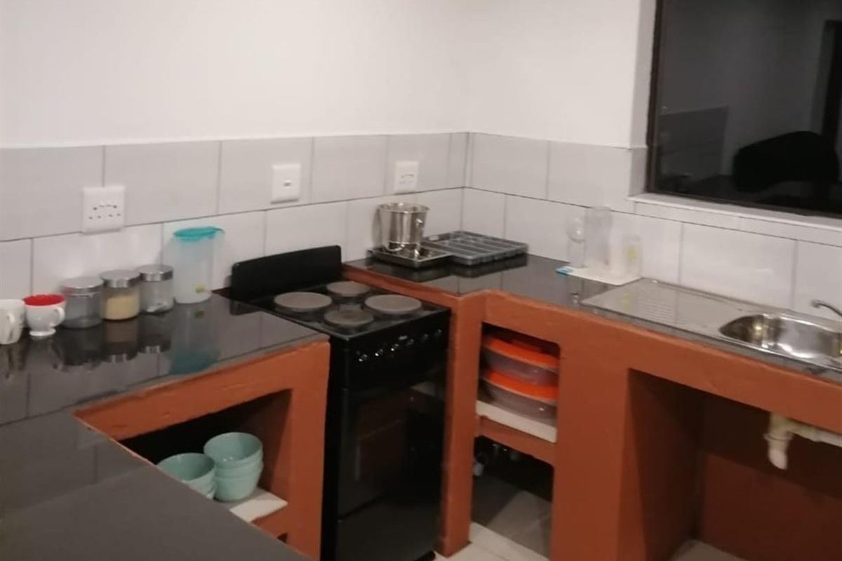 A functional kitchen area featuring dark countertops, a built-in stove, and open-shelf masonry cabinetry with tiled splashbacks.