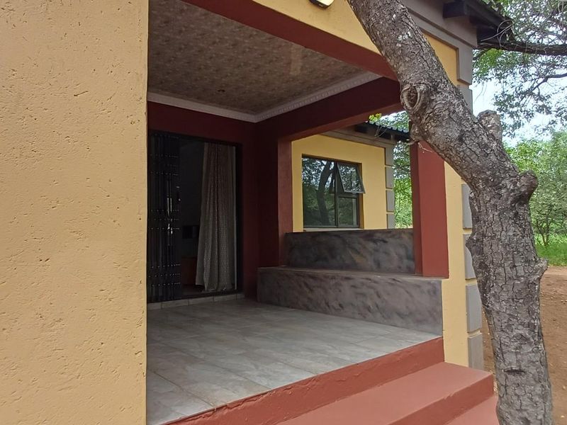 A covered patio area featuring tiled flooring, built-in concrete seating, and direct access to the interior through a sliding door.