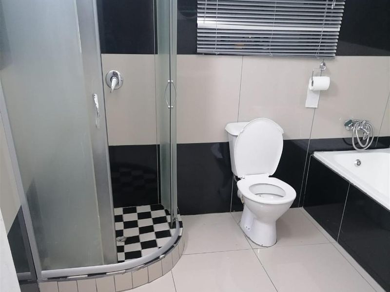Modern bathroom featuring a glass-enclosed corner shower, a built-in bathtub, and a toilet with high-contrast black and white wall tiling.