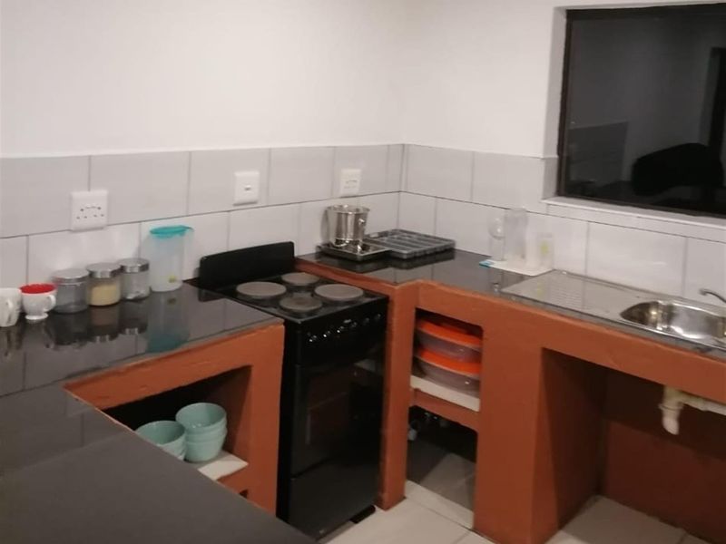 A functional kitchen area featuring dark countertops, a built-in stove, and open-shelf masonry cabinetry with tiled splashbacks.