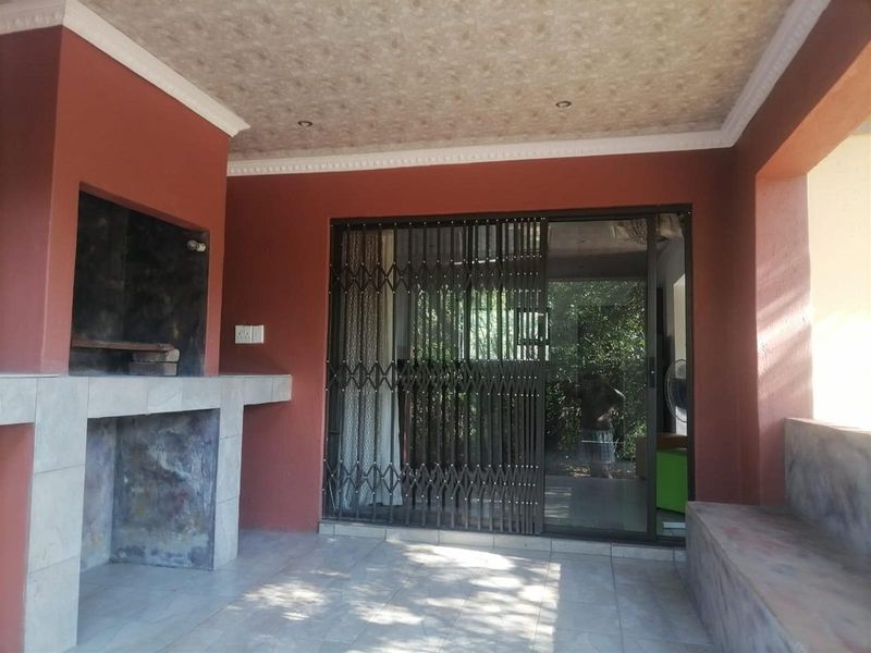 Covered patio area featuring a built-in braai, tiled flooring, and a security gate leading to the interior living space.