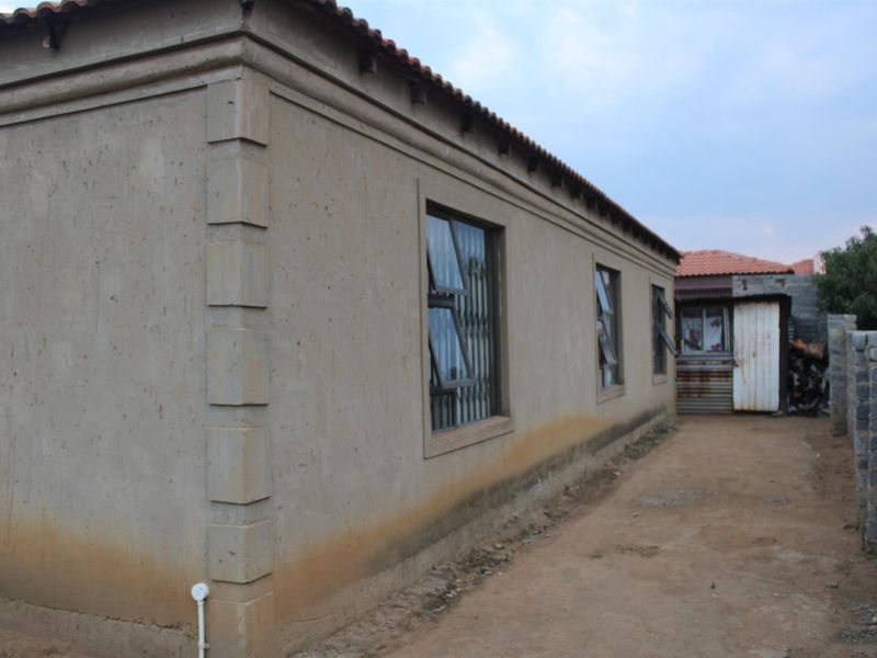 Side view of the house showing the exterior wall, window frames with security bars, and a dirt pathway leading to the rear yard.
