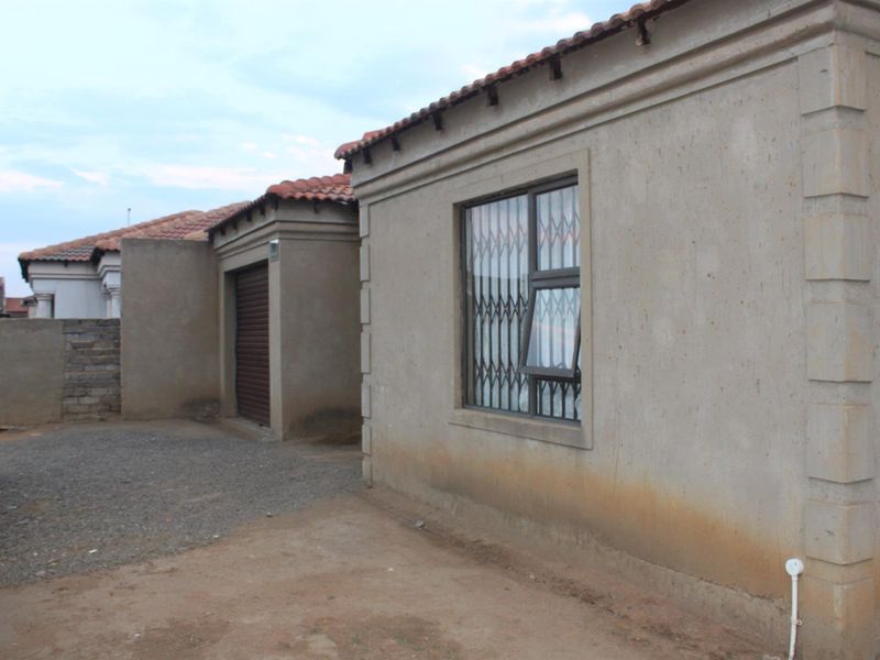 Exterior view of the property showing the side facade, garage entrance, and unpaved yard area with security bars on the window.