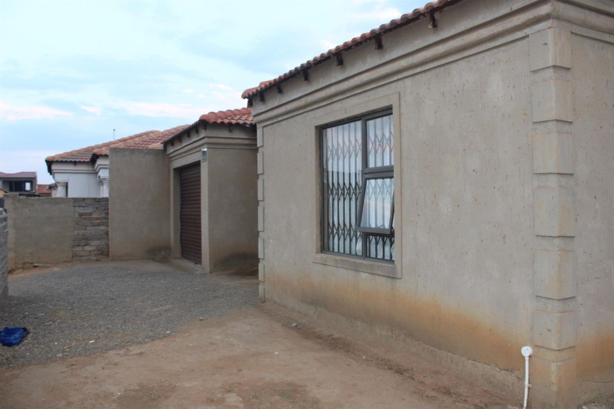 Exterior view of the property showing the side facade, garage entrance, and unpaved yard area with security bars on the window.